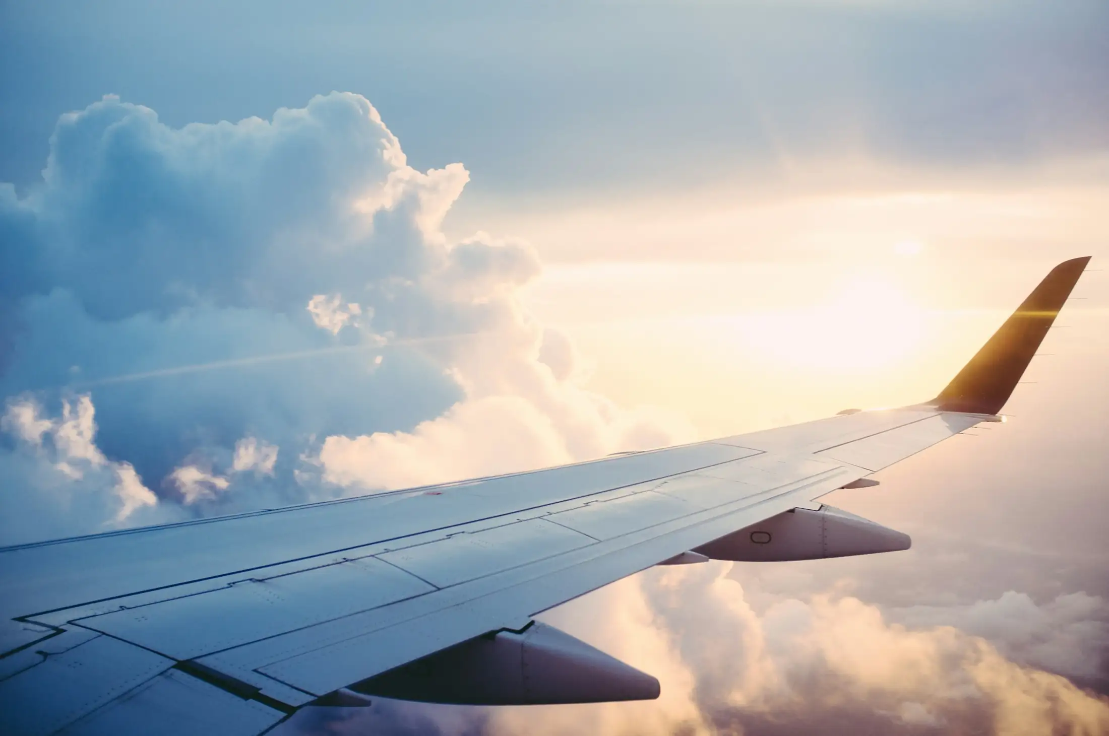 Commercial aircraft wing over clouds at sunrise on long-haul route